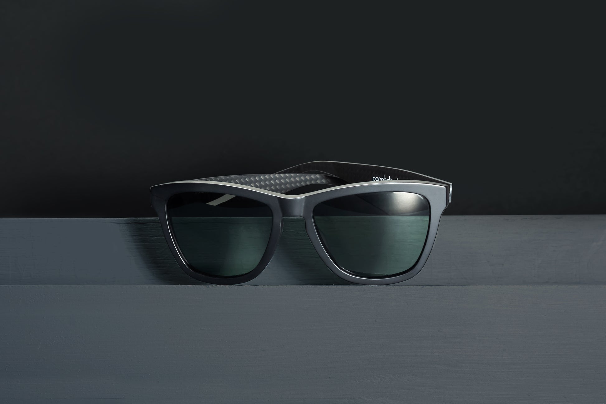 Parabolica Silverstone carbon fiber sunglasses, matte black with green polarized lenses, studio.